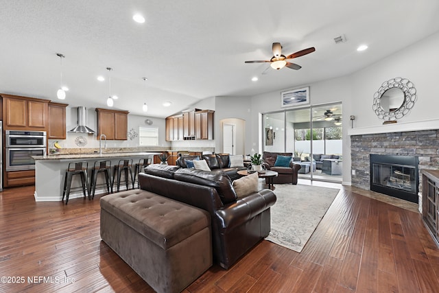 living room with lofted ceiling, visible vents, dark wood finished floors, and a stone fireplace