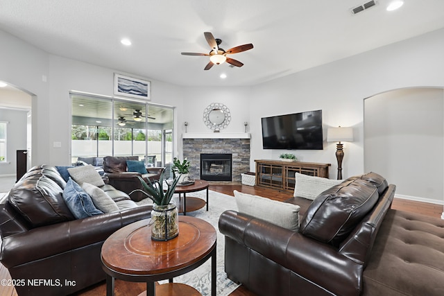 living room with visible vents, arched walkways, ceiling fan, a stone fireplace, and recessed lighting