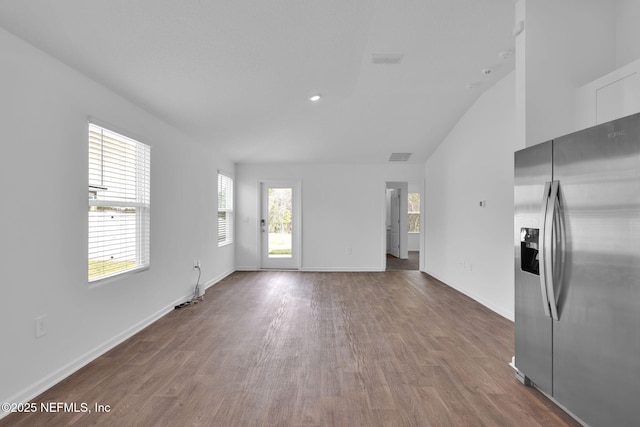 unfurnished living room featuring a towering ceiling, visible vents, baseboards, and wood finished floors