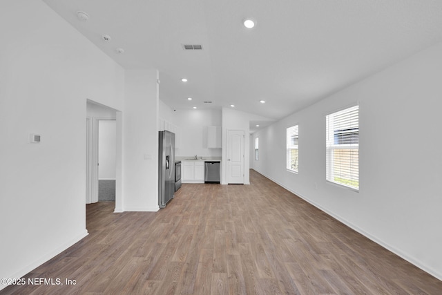 unfurnished living room featuring lofted ceiling, recessed lighting, light wood-style floors, a sink, and baseboards