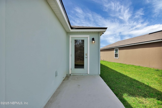 entrance to property featuring a yard, a patio, and stucco siding