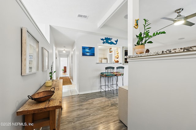 corridor with beamed ceiling, wood finished floors, visible vents, and baseboards