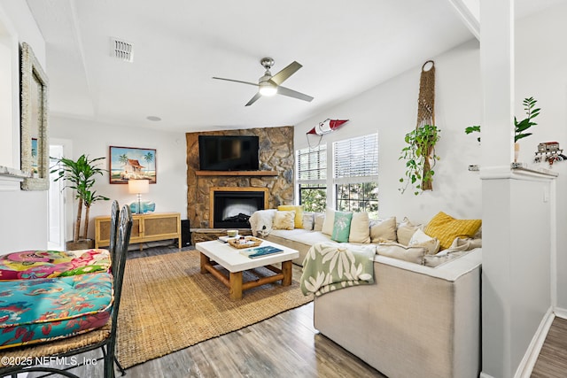 living area with visible vents, a stone fireplace, wood finished floors, and a ceiling fan