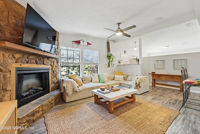 living area featuring ceiling fan, visible vents, a fireplace, and wood finished floors