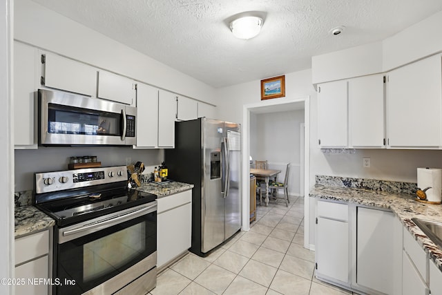 kitchen featuring light tile patterned floors, stainless steel appliances, a textured ceiling, and white cabinetry