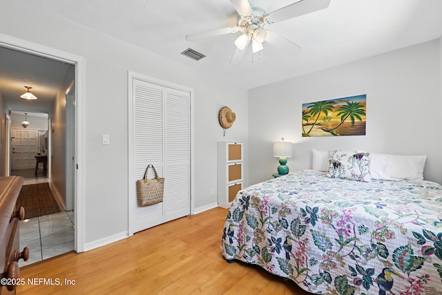 bedroom featuring ceiling fan, visible vents, baseboards, light wood-style floors, and a closet