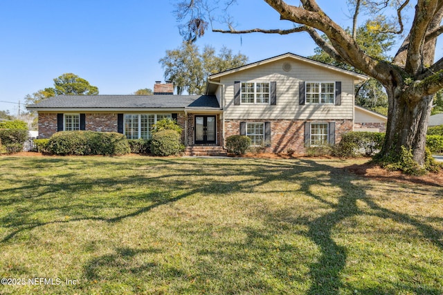 split level home with french doors, brick siding, a chimney, and a front lawn