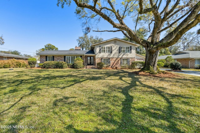 tri-level home with brick siding, a chimney, and a front yard