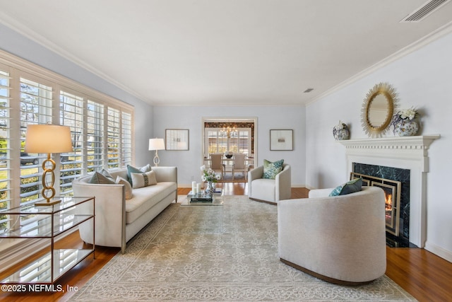 living room with a premium fireplace, wood finished floors, visible vents, baseboards, and crown molding