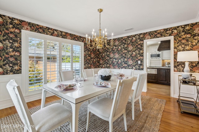 dining room with wallpapered walls, visible vents, wainscoting, an inviting chandelier, and light wood-type flooring