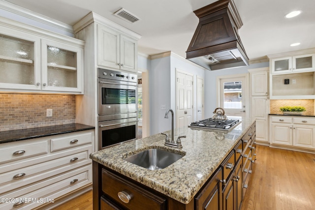 kitchen with visible vents, appliances with stainless steel finishes, light wood-style floors, premium range hood, and a sink