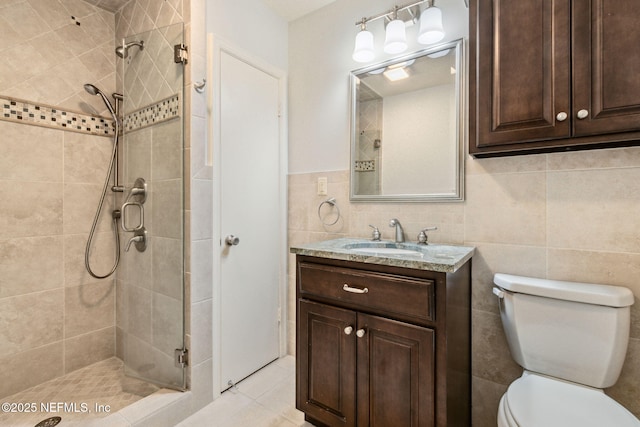 bathroom with a stall shower, toilet, tile patterned floors, vanity, and tile walls