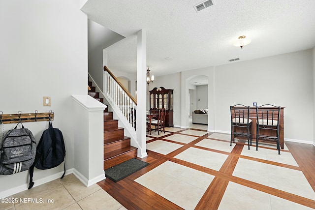 foyer entrance with arched walkways, a textured ceiling, visible vents, and baseboards