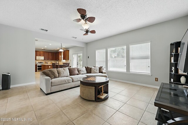 living area with light tile patterned floors, ceiling fan, a textured ceiling, visible vents, and baseboards