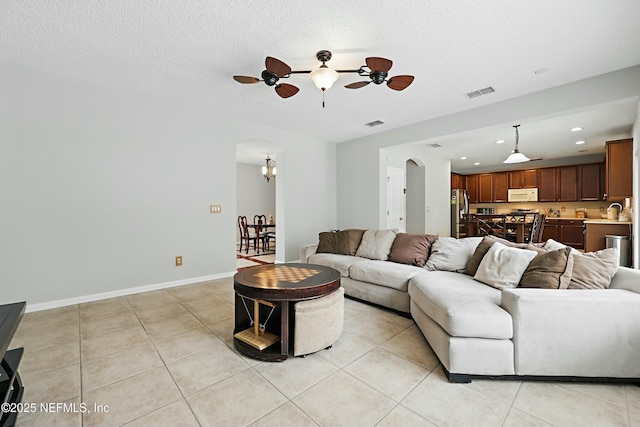 living area with arched walkways, light tile patterned floors, visible vents, and baseboards