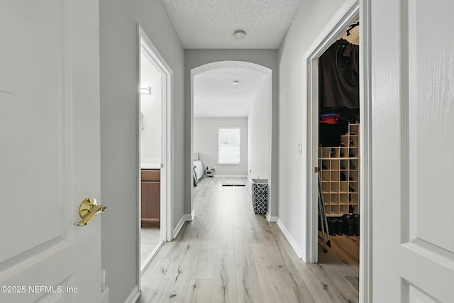 hallway with light wood-type flooring, baseboards, arched walkways, and a textured ceiling