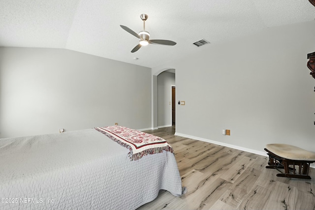 bedroom featuring arched walkways, a textured ceiling, wood finished floors, visible vents, and vaulted ceiling