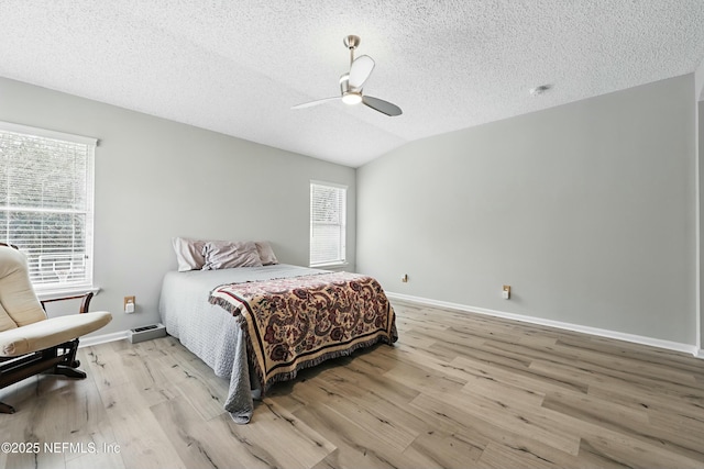 bedroom featuring lofted ceiling, light wood-style floors, baseboards, and a textured ceiling