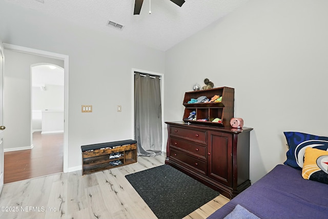 bedroom featuring arched walkways, visible vents, light wood-style floors, ceiling fan, and a textured ceiling