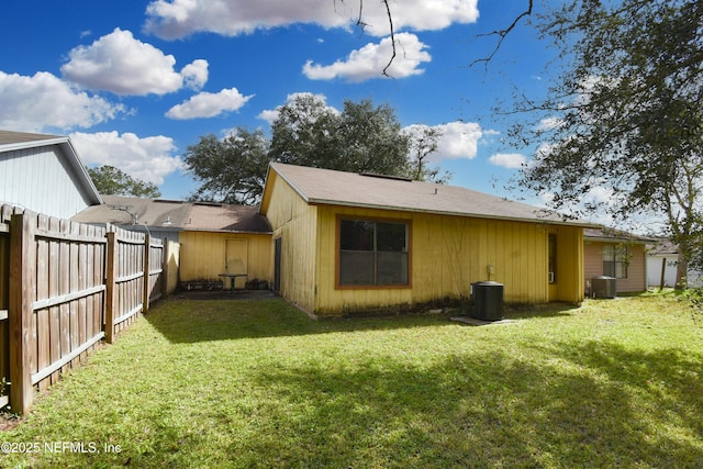 rear view of property featuring central AC unit, fence, and a lawn