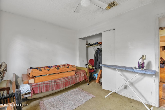 carpeted bedroom with a textured ceiling, a closet, visible vents, and a ceiling fan