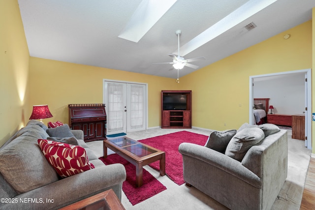 living area with vaulted ceiling with skylight, visible vents, baseboards, ceiling fan, and french doors