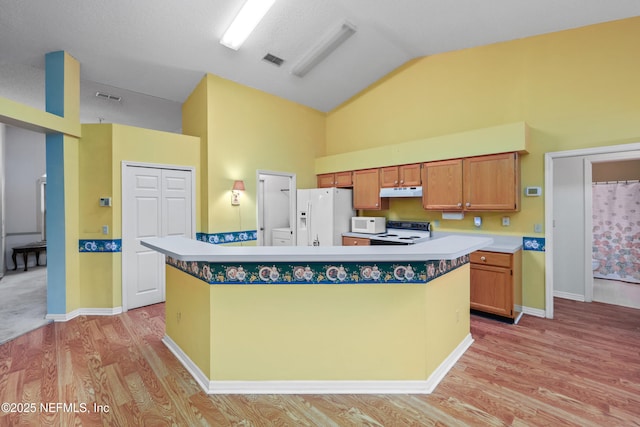 kitchen with white appliances, visible vents, a kitchen island, light countertops, and light wood-type flooring