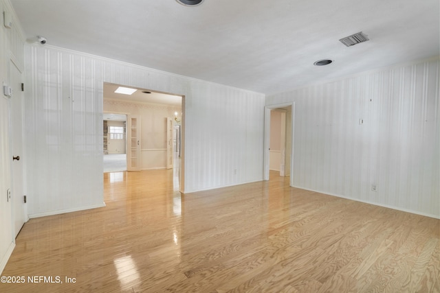 unfurnished room with light wood-style floors, baseboards, visible vents, and ornamental molding