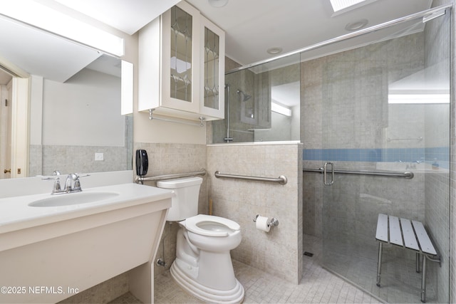 full bathroom featuring a stall shower, wainscoting, toilet, a sink, and tile walls