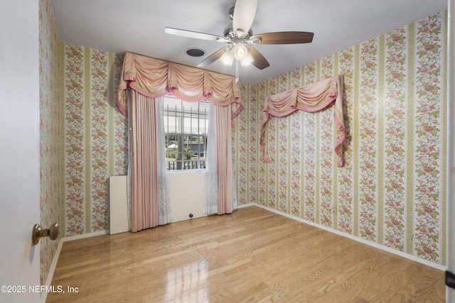 empty room featuring baseboards, wood finished floors, and wallpapered walls