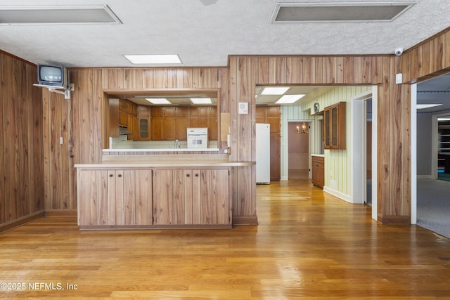 kitchen featuring glass insert cabinets, white appliances, light countertops, and light wood finished floors