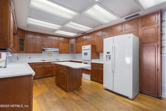 kitchen featuring visible vents, light wood-style floors, a sink, white appliances, and under cabinet range hood