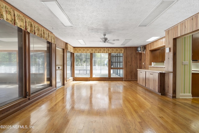 interior space with a skylight, ceiling fan, a textured ceiling, light wood-type flooring, and wood walls