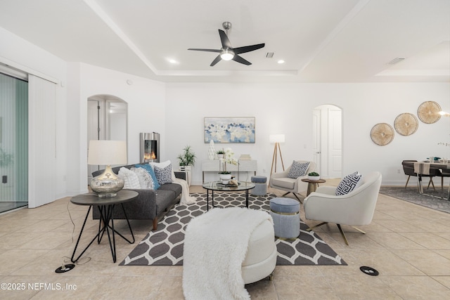 living room with arched walkways, light tile patterned floors, a raised ceiling, and visible vents