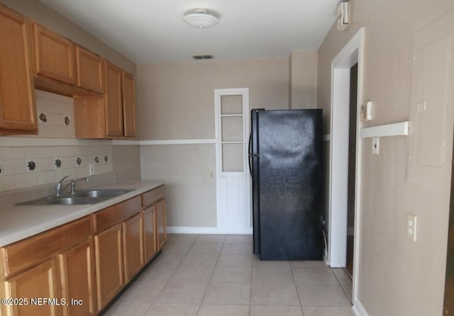 kitchen featuring decorative backsplash, freestanding refrigerator, light countertops, a sink, and light tile patterned flooring