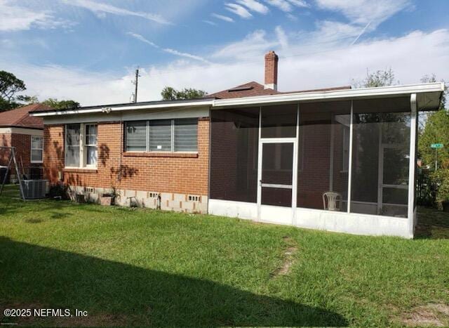 rear view of house featuring brick siding, a yard, a chimney, a sunroom, and crawl space