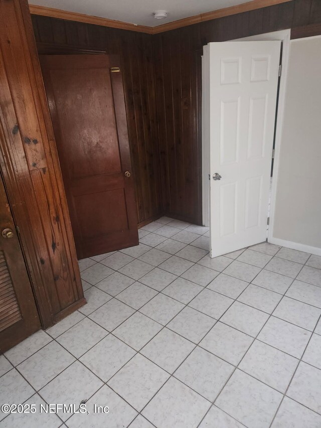 unfurnished bedroom featuring light tile patterned floors, crown molding, wooden walls, and a closet