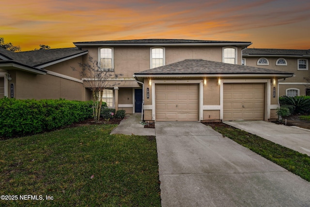 traditional-style house with an attached garage, a yard, concrete driveway, and stucco siding