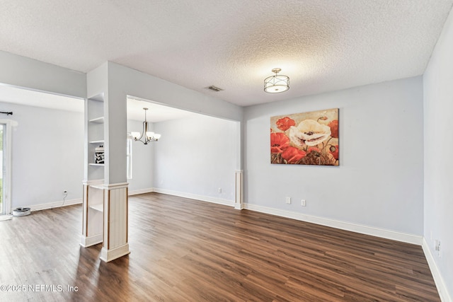 spare room featuring an inviting chandelier, baseboards, dark wood finished floors, and a textured ceiling