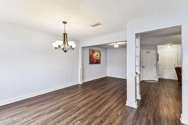 unfurnished dining area featuring a textured ceiling, a notable chandelier, dark wood-style flooring, visible vents, and baseboards