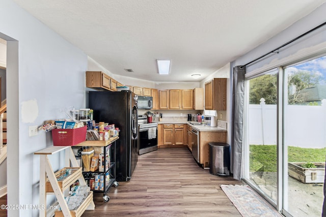 kitchen featuring light wood finished floors, light countertops, a textured ceiling, black appliances, and a sink