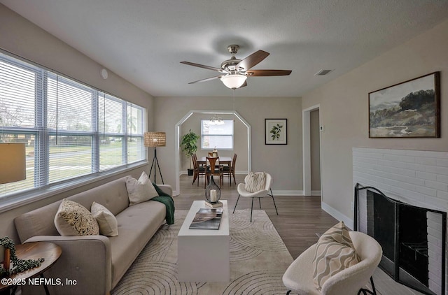 living room with arched walkways, visible vents, a brick fireplace, wood finished floors, and baseboards