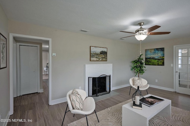 living area featuring baseboards, a fireplace, visible vents, and wood finished floors