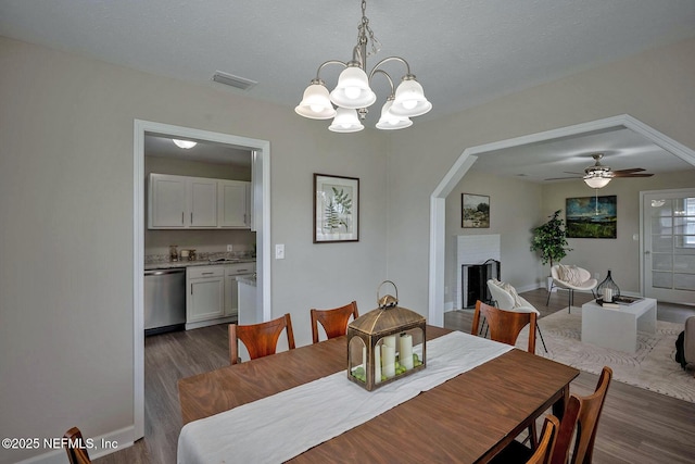 dining room with a chandelier, a fireplace, visible vents, baseboards, and dark wood-style floors