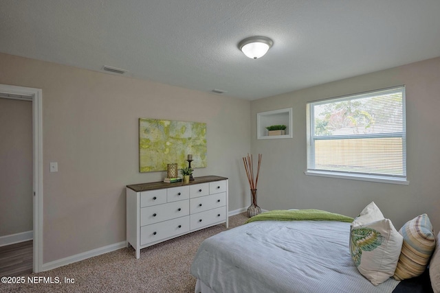 carpeted bedroom with visible vents, a textured ceiling, and baseboards