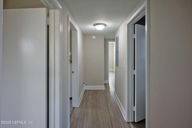 hallway with light wood-style floors, a textured ceiling, and baseboards