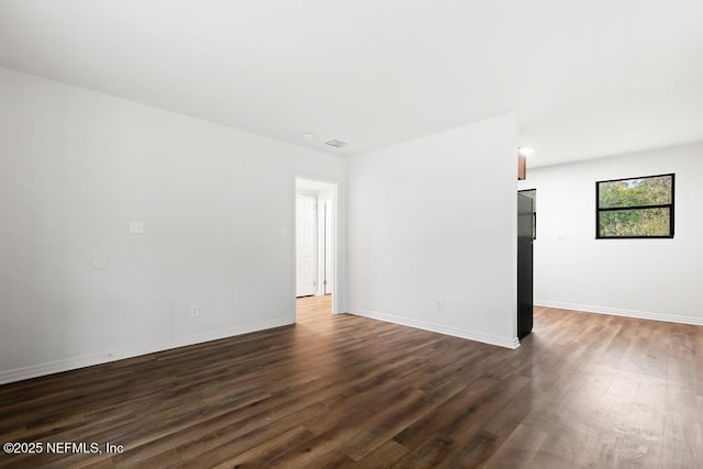 empty room featuring visible vents, baseboards, and dark wood-style flooring