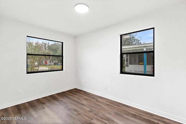 unfurnished room featuring baseboards and dark wood-type flooring