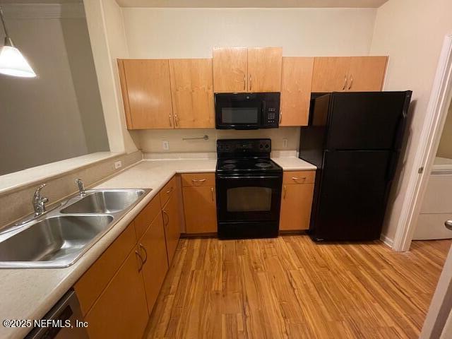 kitchen featuring a sink, black appliances, light countertops, and pendant lighting