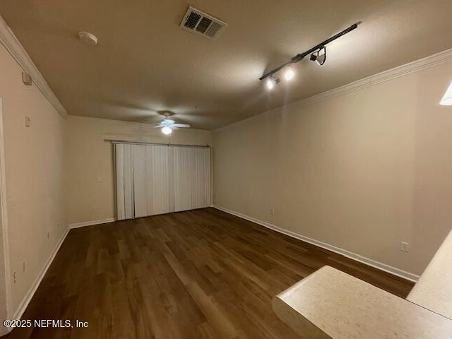 unfurnished room featuring dark wood-style flooring, visible vents, crown molding, and baseboards